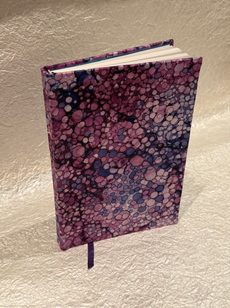 A closed journal with a colorful abstract cover featuring a pattern of purple, pink, and blue dots, against a light textured background.