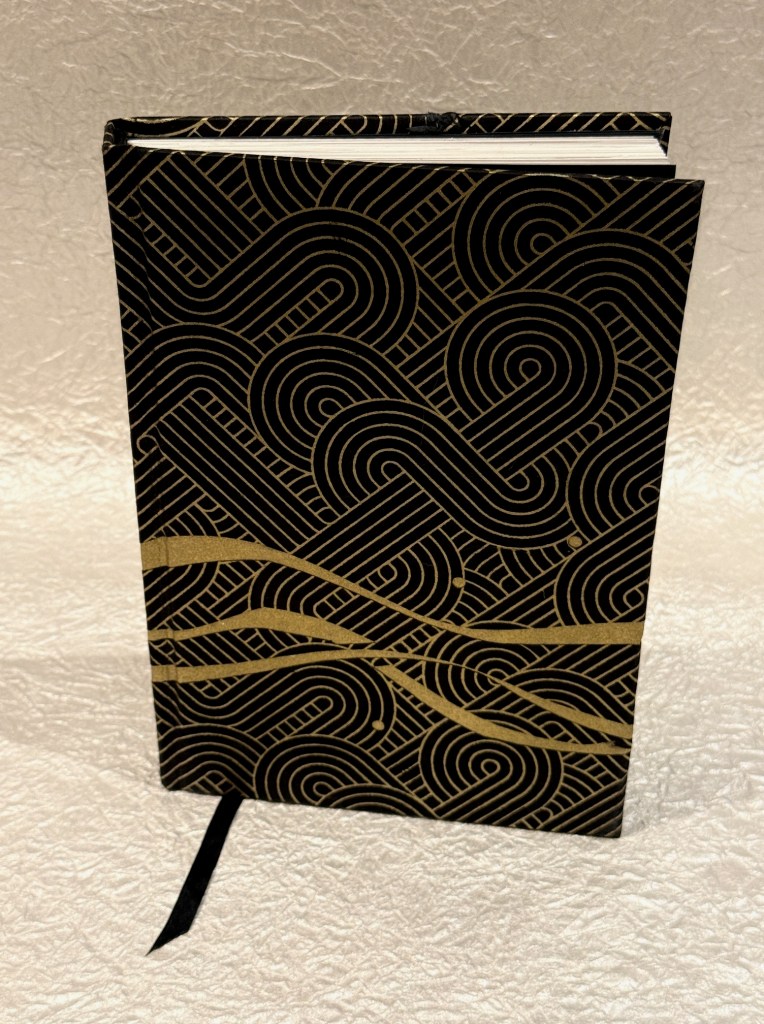A stylish black notebook with a gold geometric pattern on the cover, featuring swirling lines and shapes.