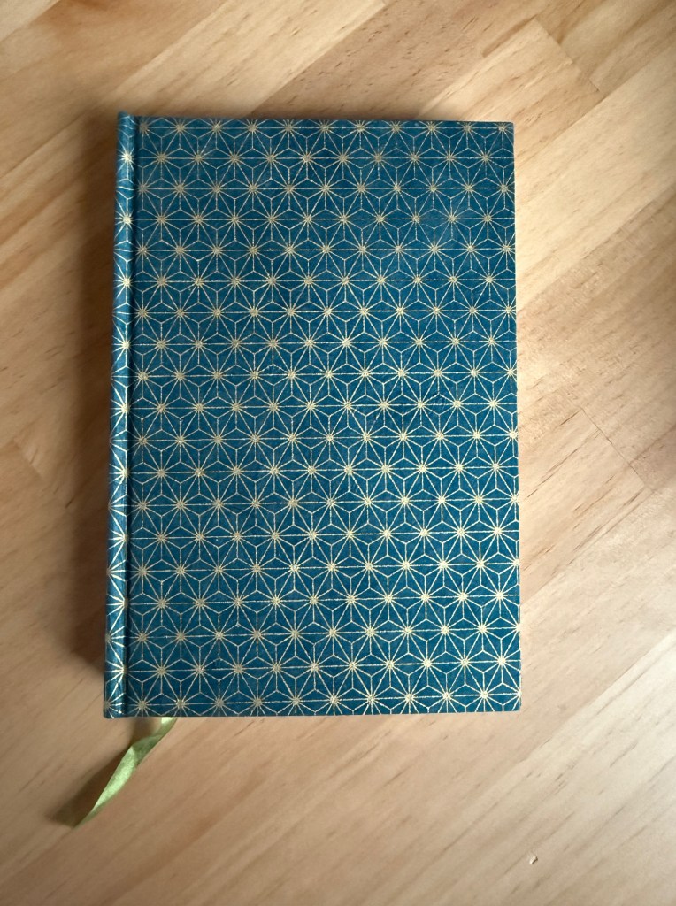 A closed notebook with a blue cover featuring a geometric gold star pattern, resting on a wooden surface.