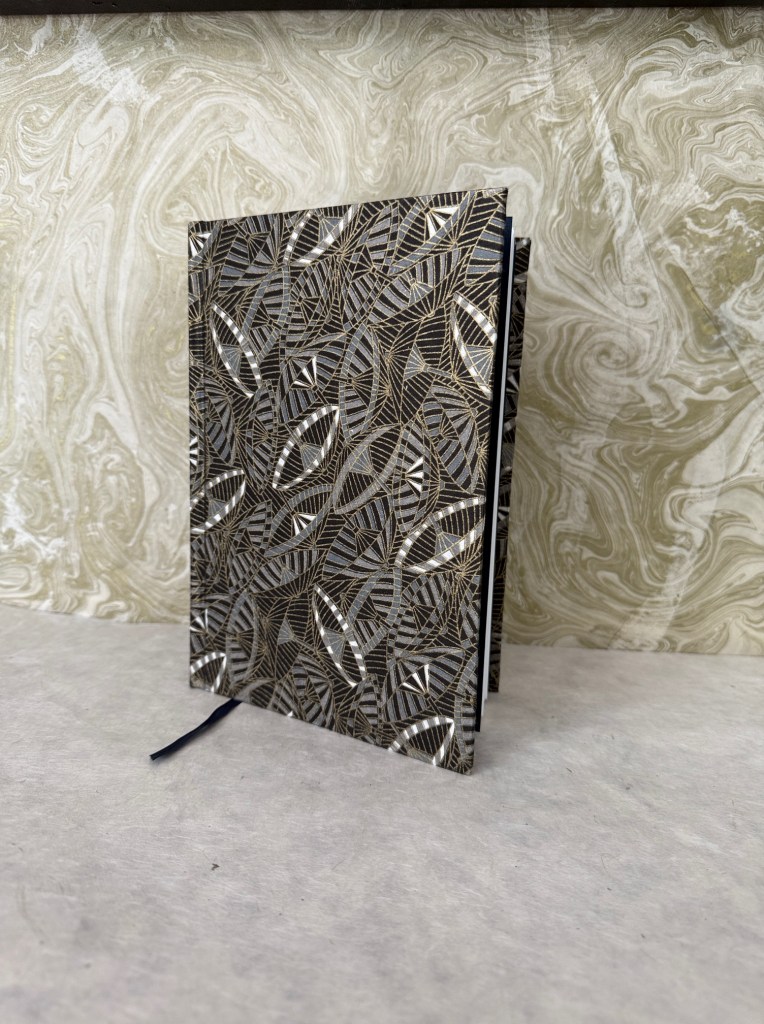 A decorative journal with an intricate geometric design on the cover, featuring metallic accents, placed on a textured background.