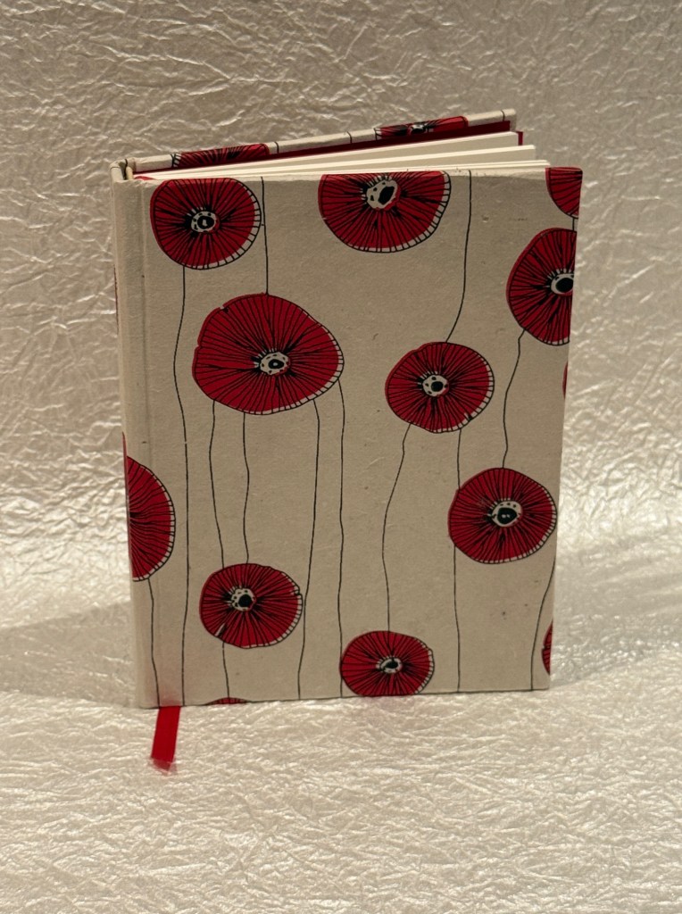 A closed notebook with a cover decorated with red poppies on a light background, featuring a red ribbon bookmark.