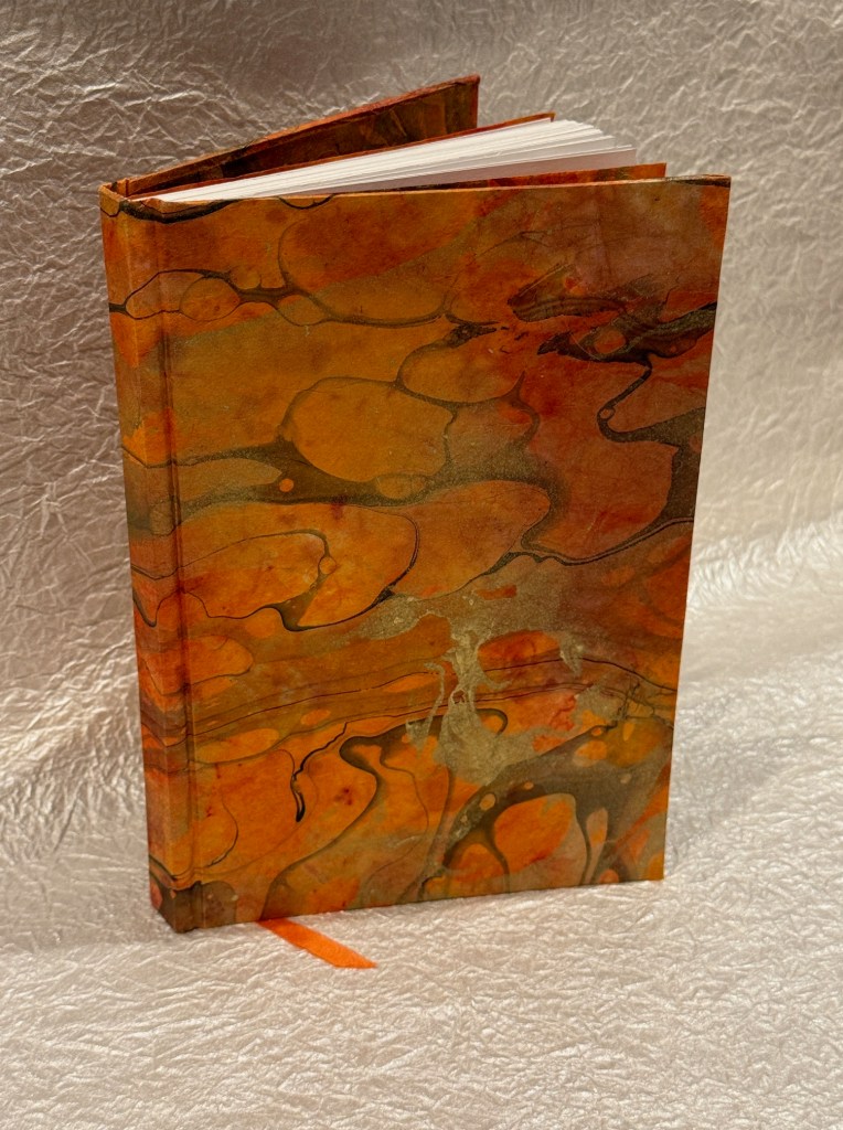A marbled hardcover book with an orange and gold design, partially open to reveal the blank pages inside.